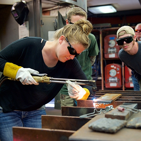Lady welder uses acetylene torch as other students observe